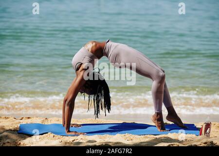 Woman doing wheel yoga pose on the beach hi-res stock