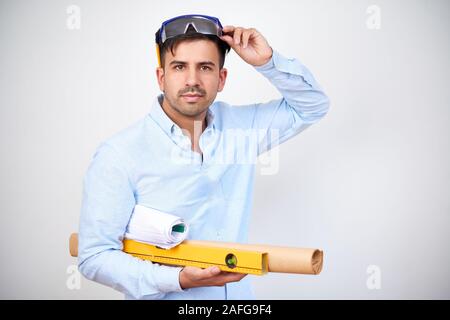 Head engineer with construction level and blueprint taking off goggles and looking at camera Stock Photo