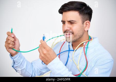Portrait of confused young man looking at patch cords of different colors Stock Photo