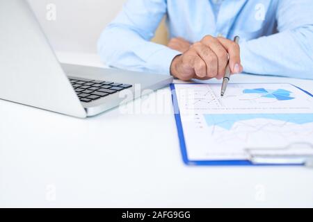 Entrepreneur sitting at office table and checking document with financial chart when working on laptop Stock Photo