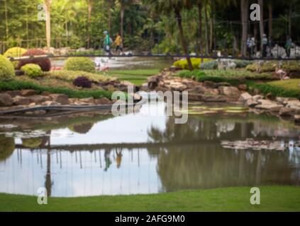 Defocused blurred image of summer nature park with people walking on rope bridge crossing river Stock Photo