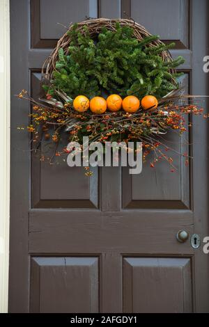 Evergreen and twig.stick Christmas wreath on brown colonial door in the historic area. Colonial Williamsburg, Virginia. Five oranges are central. Stock Photo