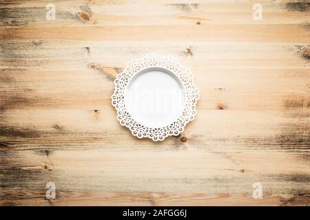 Empty, round white plate, with a beautiful carved floral pattern on the rim. Textured wood background. Stock Photo