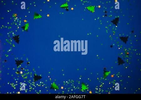 Christmas frame composition with golden star-shaped sequins and pine trees on blue holographic background. Celebration preparation concept. Selective Stock Photo