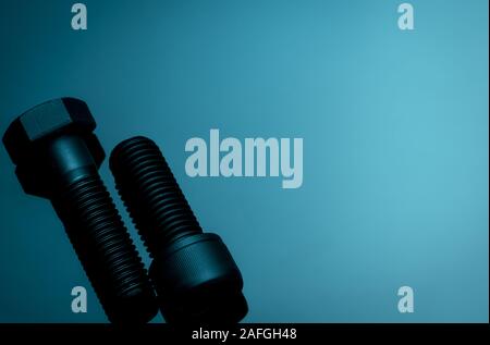 Metal bolts on blue background. Hardware tools. Closeup hex head bolt and socket cap bolt with copy space. Threaded fastener use in automotive engine Stock Photo