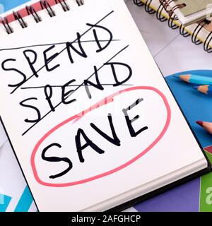 The word Save circled in red below a list of spending written on a notepad surrounded by pencils, graphs, books and calculator. Stock Photo