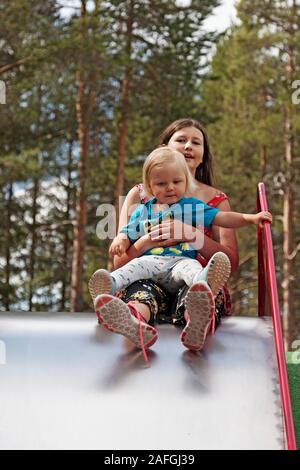 Umea, Norrland Sweden - July 29, 2019: big sister and little brother ride slide together Stock Photo