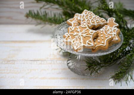 Gingerbread cookies for Christmas on a crystal glass bowl and decoration from fir branches on a white painted wooden table, copy space, selected focus Stock Photo