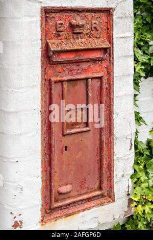 Distressed, old, disused, wall mounted, Royal Mail post box with peeling and faded red paint set into whitewashed wall, England, UK Stock Photo