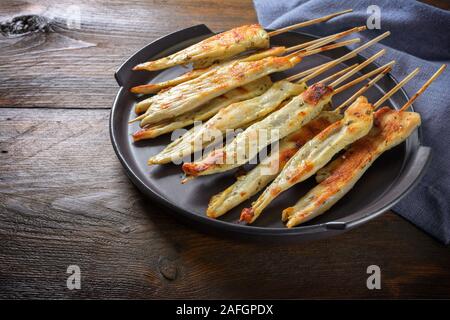Fried lemon chicken skewers with herbs and spices in mediterranean style, served as finger food on a plate for a festive party, dark rustic wooden tab Stock Photo