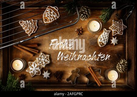 Gingerbread, burning candles and cookie cutters on a dark wooden tray, German text Frohe Weihnachten, meaning  Merry Christmas, flat lay, high angle v Stock Photo