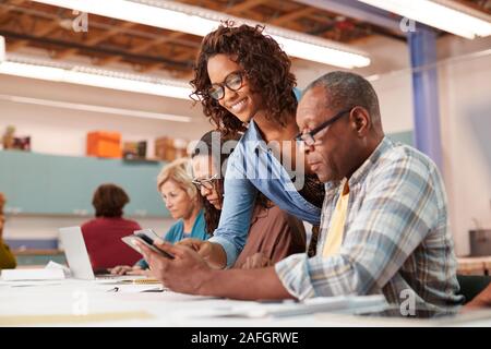 Teacher Helping Retired Senior Man Attending IT Class In Community Centre Stock Photo