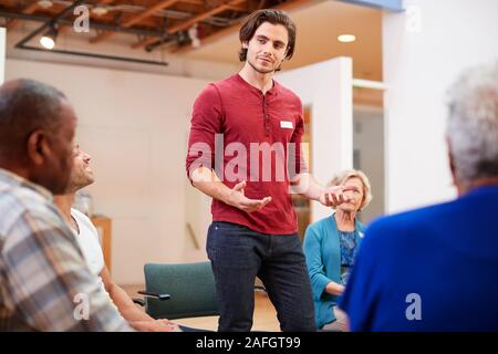 Man Standing To Address Self Help Therapy Group Meeting In Community Center Stock Photo
