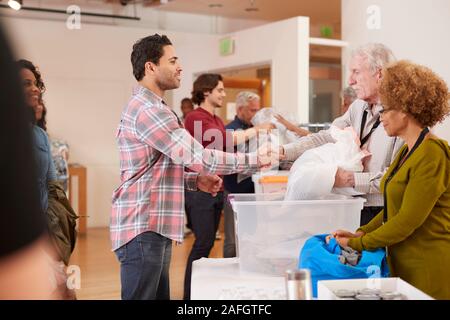 People Donating Clothing To Charity Collection In Community Center Stock Photo