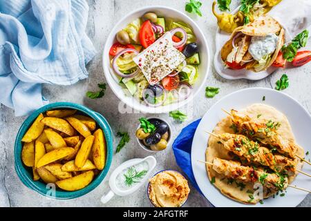 Flat lay of Greek food: greek salad, chicken souvlaki, gyro and baked potatoes on a gray background, top view. Traditional greek cuisine concept. Stock Photo