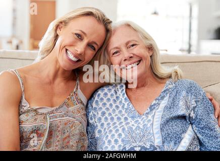 Portrait Of Smiling Mother With Adult Daughter Relaxing On Sofa At Home Stock Photo