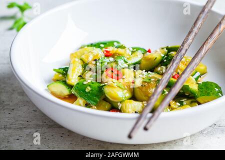 Asian beaten cucumber salad with chili and sesame seeds in a white bowl. Chinese food concept. Stock Photo