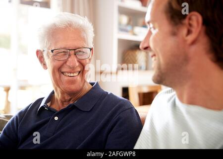 Smiling Father With Adult Son Relaxing On Sofa At Home Stock Photo