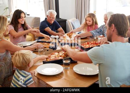 Multi Generation Family Sitting Around Table Eating Takeaway Pizza Together Stock Photo