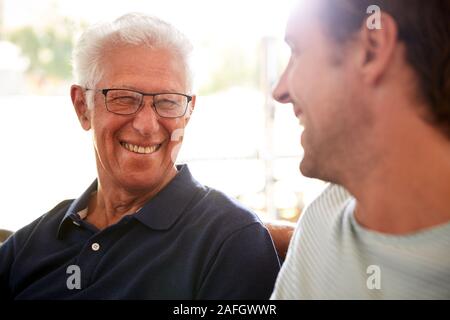 Smiling Father With Adult Son Relaxing On Sofa At Home Stock Photo