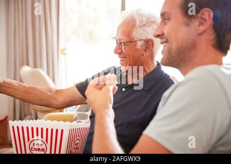 Father With Adult Son Eating Popcorn Watching Movie On Sofa At Home Together Stock Photo