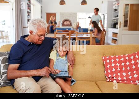 Grandfather Sitting With Granddaughter On Sofa Using Digital Tablet At Home Stock Photo