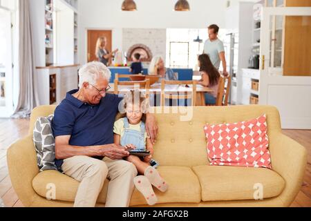 Grandfather Sitting With Granddaughter On Sofa Using Digital Tablet At Home Stock Photo