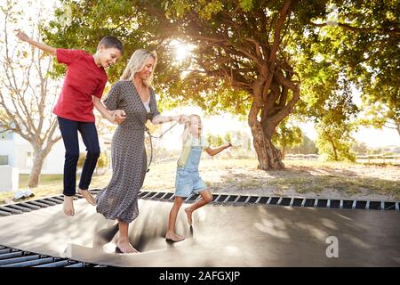 Mother Playing With Children On Outdoor Trampoline In Garden Stock Photo