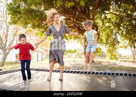 Mother Playing With Children On Outdoor Trampoline In Garden