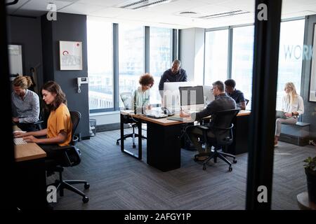 Young creative team working together at computers in a casual office, seen from doorway Stock Photo