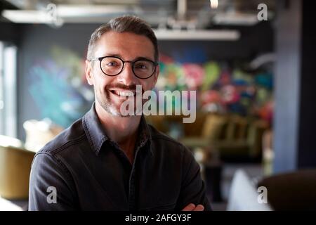 Middle aged white male creative in casual office lounge area looks to camera smiling, close up Stock Photo
