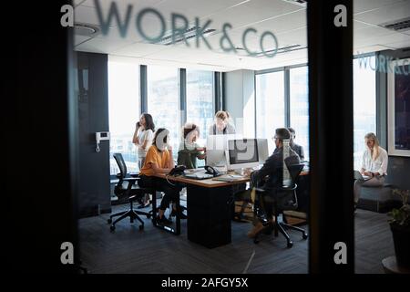 Creative business team working in a casual office, seen through glass wall with text on it Stock Photo
