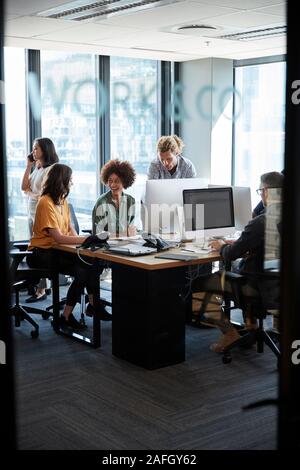 Creative colleagues in working in a casual office, seen through glass wall with text on it, vertical Stock Photo