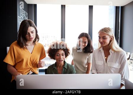 Four female creatives working around a computer monitor in an office, front view, close up Stock Photo