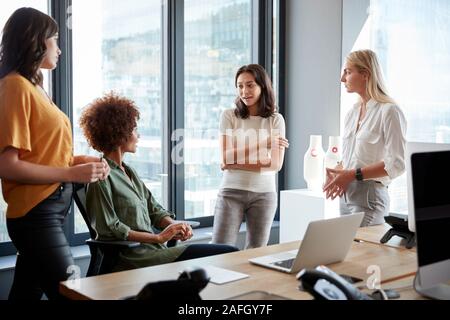 Four female colleagues in discussion at a desk in a creative office, three quarter length Stock Photo