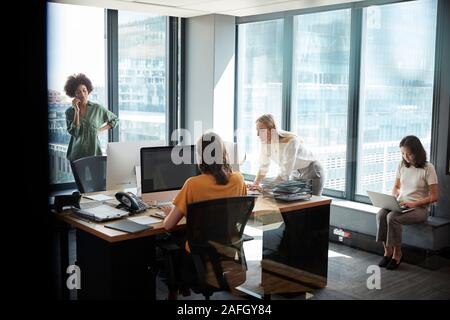 Four female creative colleagues working together in an office, seen through glass with reflection Stock Photo