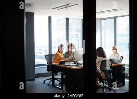 Four female creative colleagues busy working in an office, seen through glass wall with text on it Stock Photo