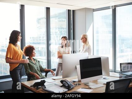 Four female colleagues in discussion at a desk in a creative office, looking at each other Stock Photo
