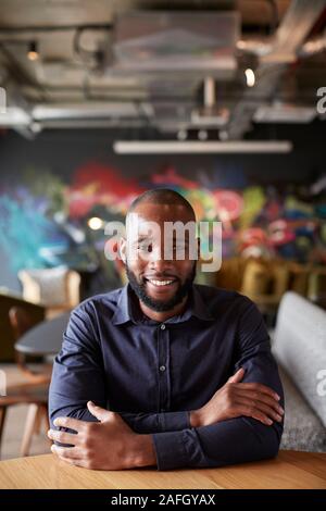 Mid adult black male creative sitting at a table with arms crossed smiling to camera, close up Stock Photo