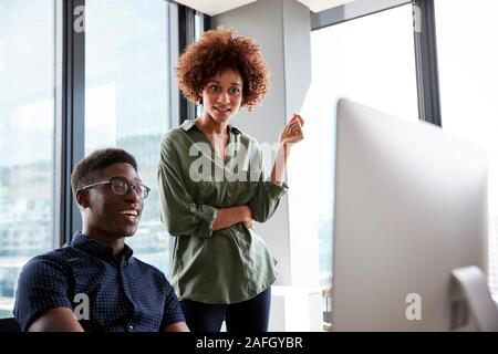 A male and female creative working together at a desk looking at a computer monitor, close up Stock Photo