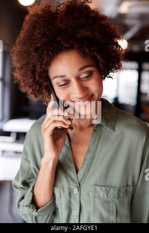 Millennial black female creative in an office using smartphone, looking down, close up, vertical Stock Photo