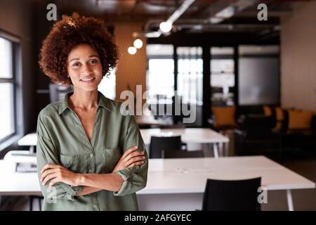 Millennial black female creative standing in an open plan office with arms crossed smiling to camera Stock Photo