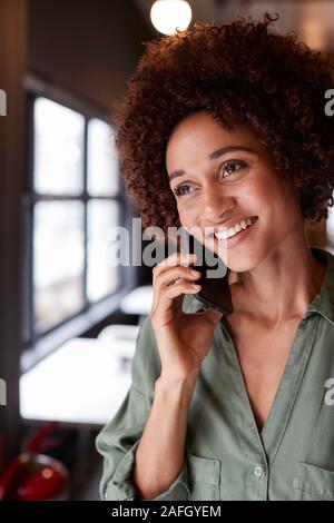 Millennial black female creative standing in an office using smartphone, close up, vertical Stock Photo