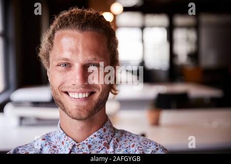 Millennial white male creative sitting in an office smiling to camera, head and shoulders close up Stock Photo