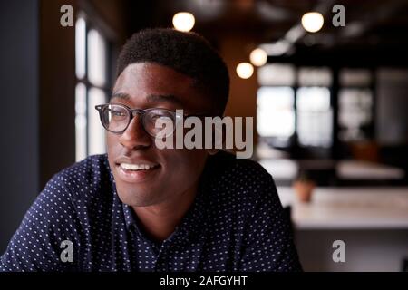 Young black male creative sitting at a desk in an office looking out of the window smiling, close up Stock Photo