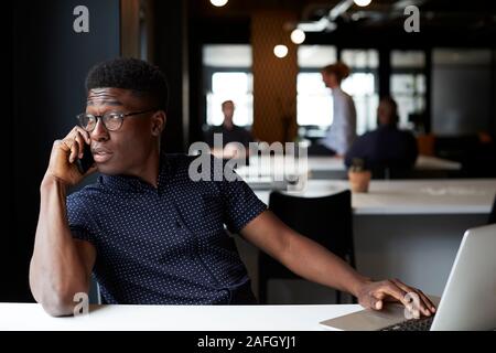 Millennial black male creative sitting in an office looking out of the window using phone, close up