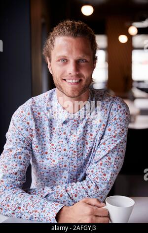 Millennial white male creative sitting at a desk in an open plan office smiling to camera, vertical Stock Photo