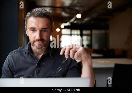 Middle aged white male creative looking at laptop screen in an office, holding glasses, close up Stock Photo