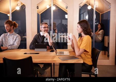 Creative colleagues sitting at a table drinking coffee and talking in their office canteen, close up Stock Photo