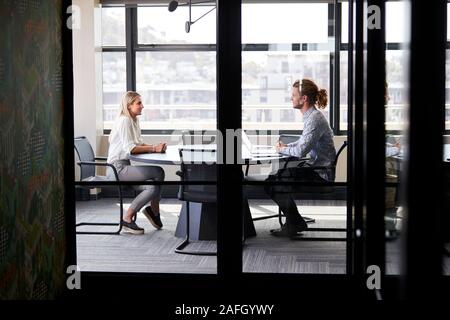 Two millennial business creatives in a meeting room for a job interview, seen through glass wall Stock Photo